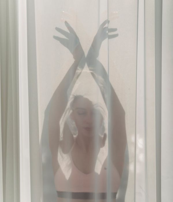 Woman performing a gentle yoga pose in a dark room with mint green light.